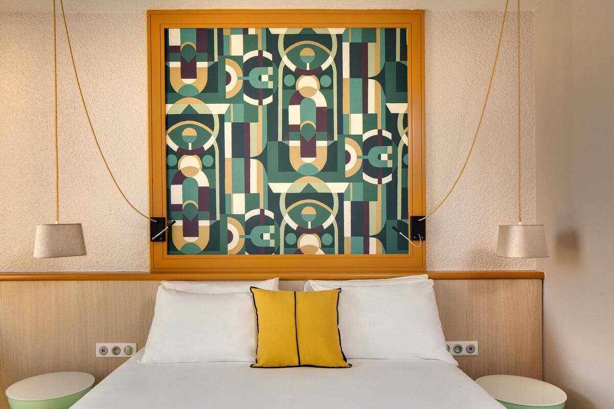 Habitación de hotel con una cama, dos mesitas de noche, una obra de arte en la pared y un aplique de techo.