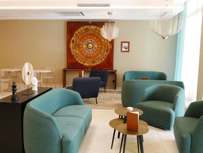 Un salón moderno con sillones azul verdosos, un tablero de ajedrez y una gran obra de arte circular en la pared.
