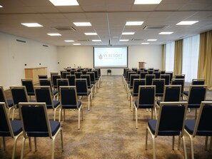A conference room with rows of chairs, a podium, a screen with 'WYRESORT THERMAL & SPA' text, and a patterned carpet.