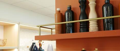 A shelf with various bottles and a wooden object, possibly a salt shaker, against a wall.