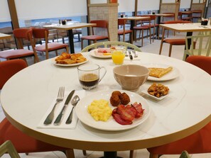 A breakfast setting with plates of scrambled eggs, bacon, croissants, and a bowl of cereal.