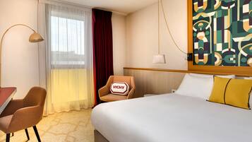 Una habitación de hotel con cama, escritorio, silla, ventana con cortinas y un cuadro en la pared.