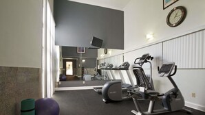 A gym with exercise equipment, a large mirror, and a clock on the wall.