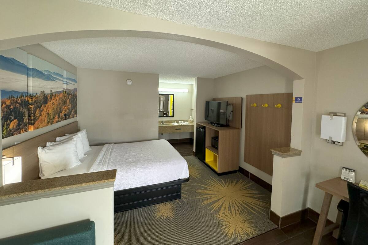 Ein Hotelzimmer mit Bett, Schreibtisch, Fernseher und einem durch einen Bogen führenden Durchgang sichtbarem Badezimmer.