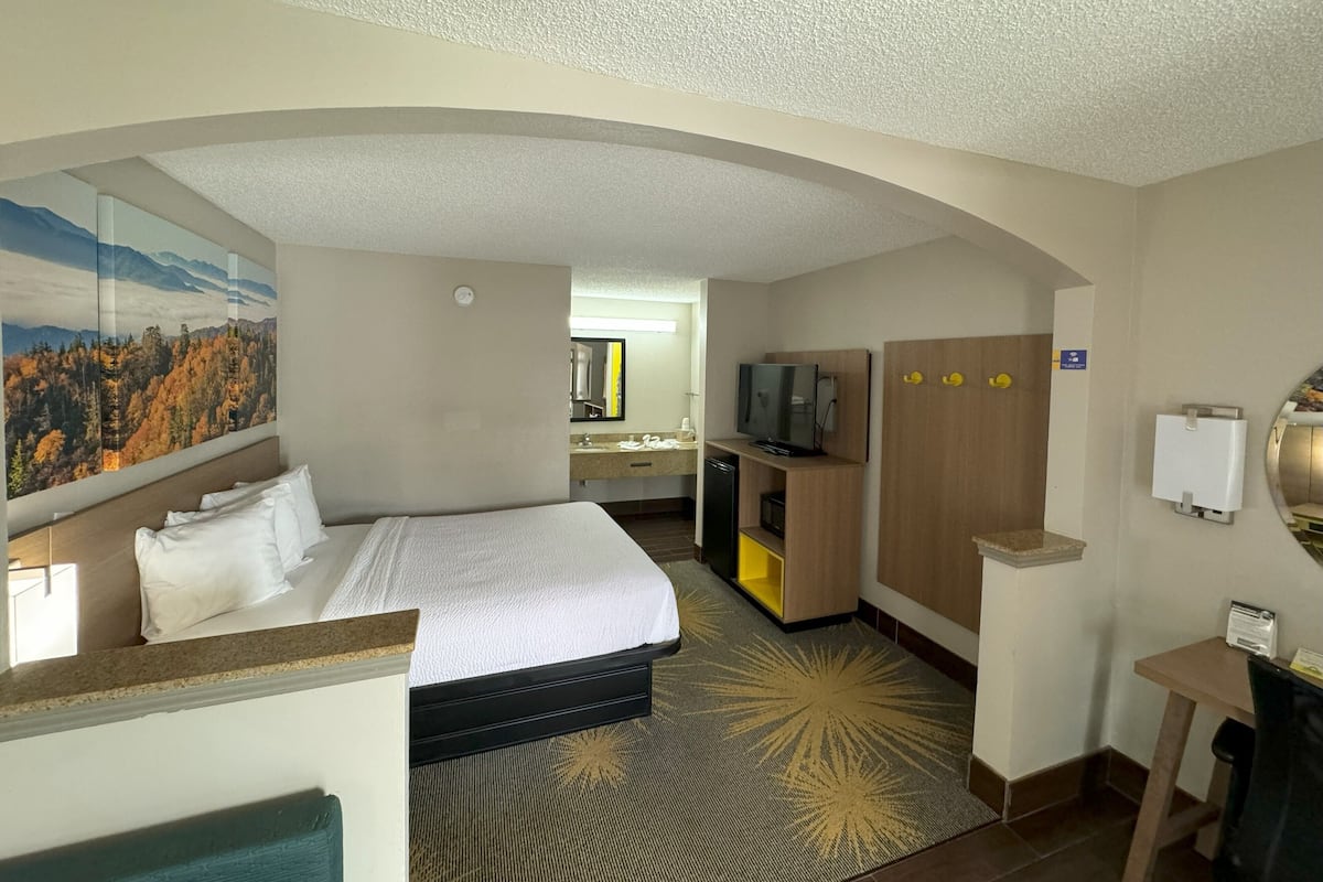 A hotel room with a bed, a desk, a television, and a bathroom visible through an arched doorway.