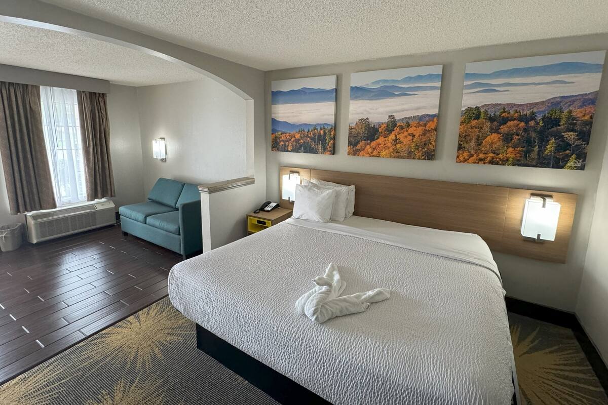 Ein Hotelzimmer mit einem großen Bett, einer Sitzecke, einem Schreibtisch und einem Fenster mit Vorhängen.