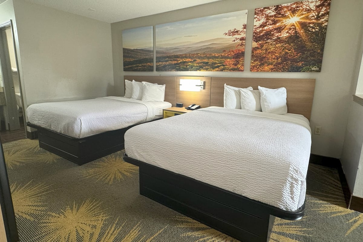 A hotel room with two beds, a nightstand, a phone, and a wall-mounted light.