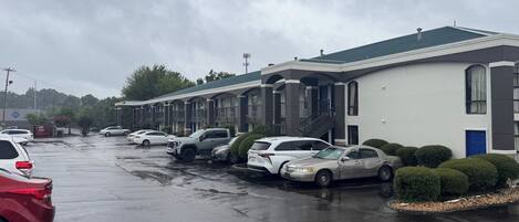 A motel with a row of parked cars, a covered walkway, and a blue door on the right.