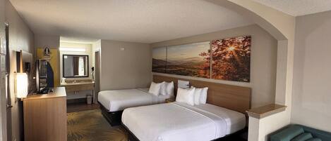 A hotel room with two beds, a desk, a mirror, and a painting on the wall.