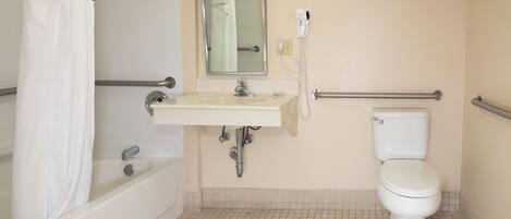 Une salle de bain avec un lavabo, un miroir et des toilettes blancs. On y trouve un rideau de douche et un sèche-mains.