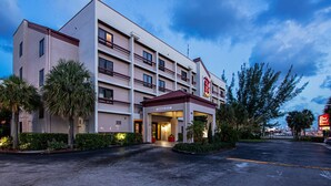 A multi-story hotel with a central entrance, palm trees, and a parking lot.