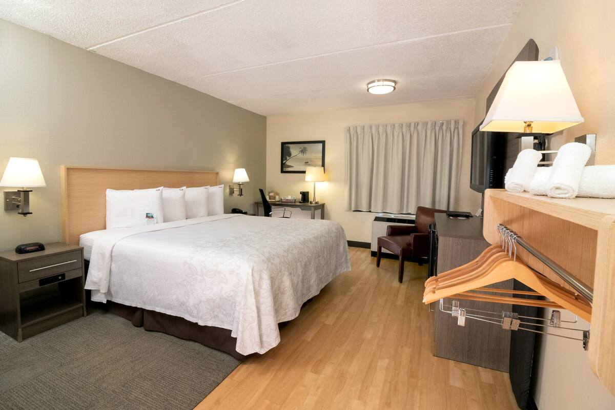 A hotel room with a large bed, bedside lamps, a desk with a chair, and a coat rack with hangers.