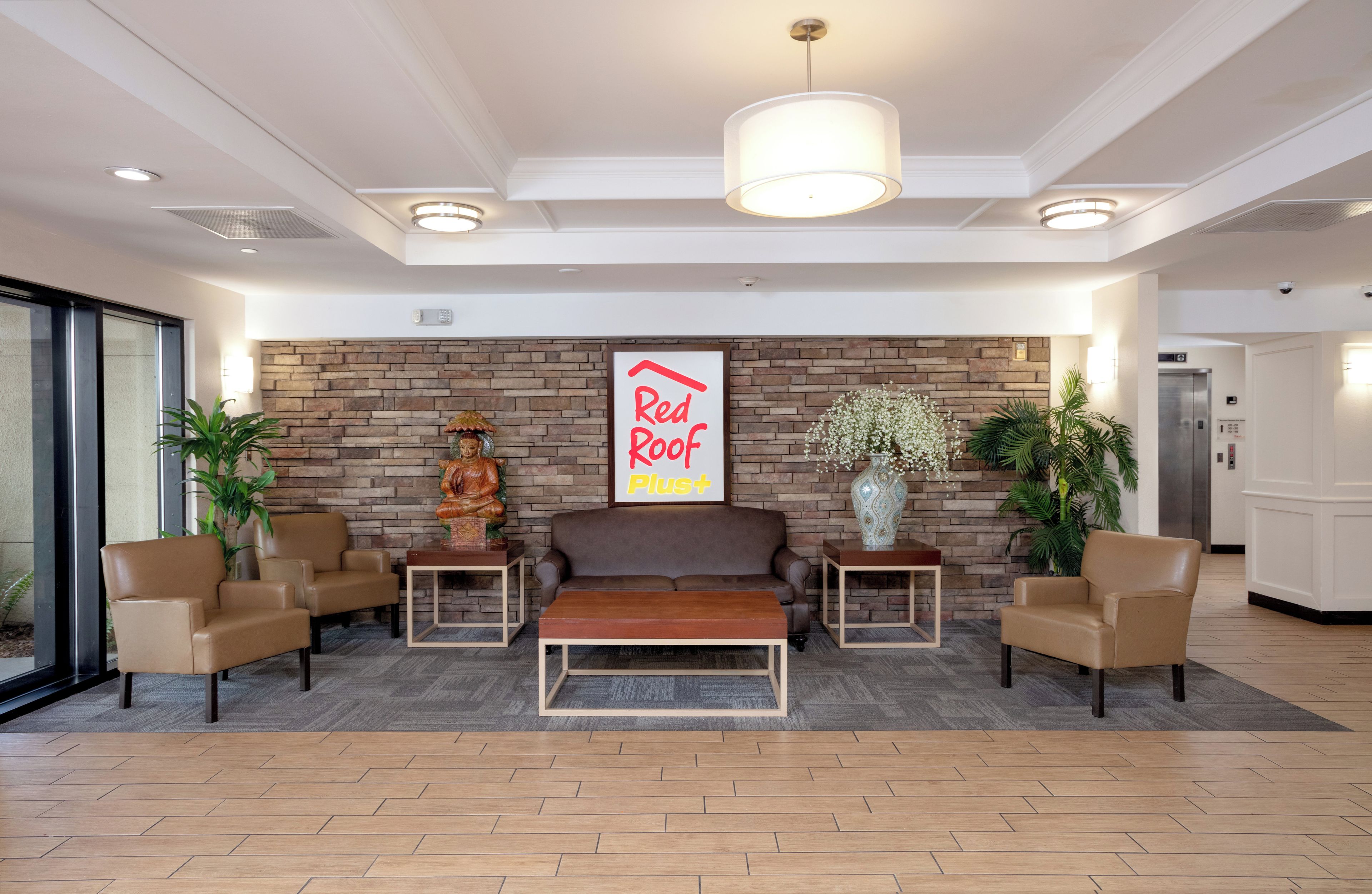 A lobby with a sofa, chairs, a red-roof sign, a statue, and a vase.