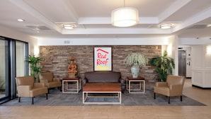 A lobby with a sofa, chairs, a coffee table, a wall-mounted Buddha statue, a 'Red Roof Plus' sign, and a stone wall. - Red Roof Inn PLUS+ Miami Airport (Miami)