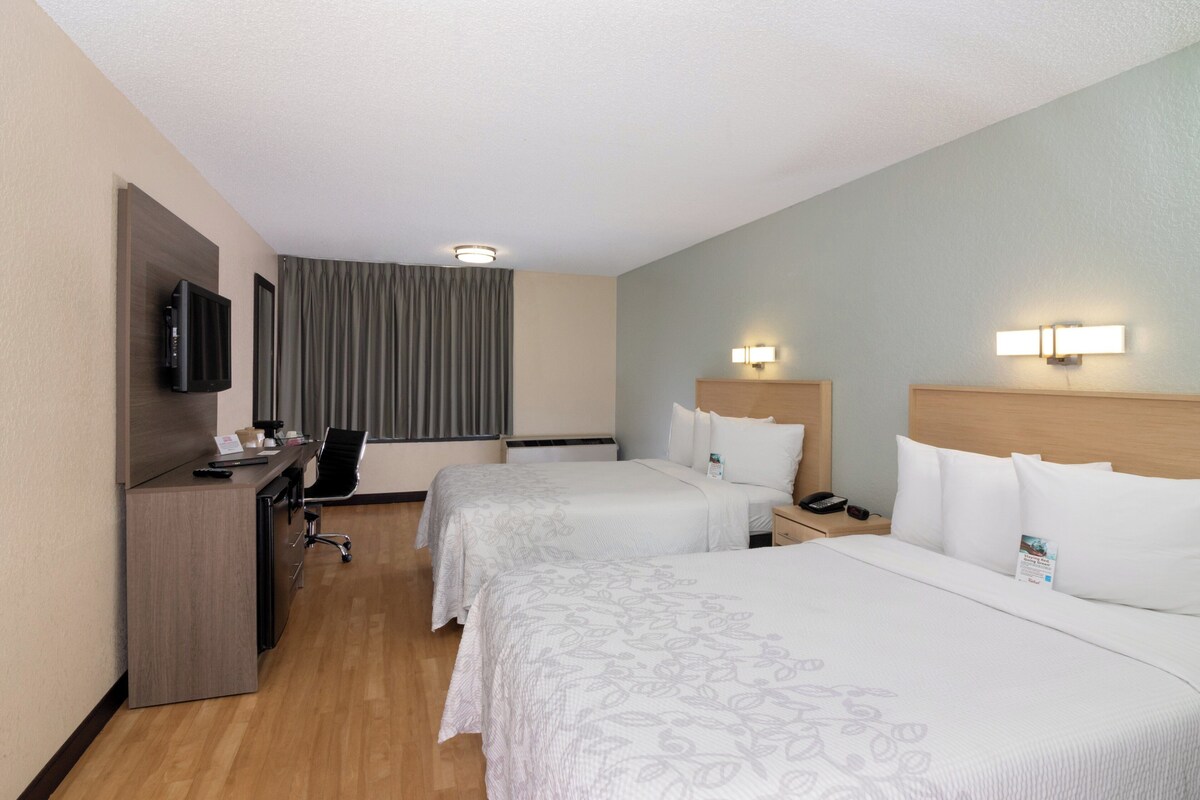 A hotel room with two beds, a desk with a TV, a chair, and a window with curtains.