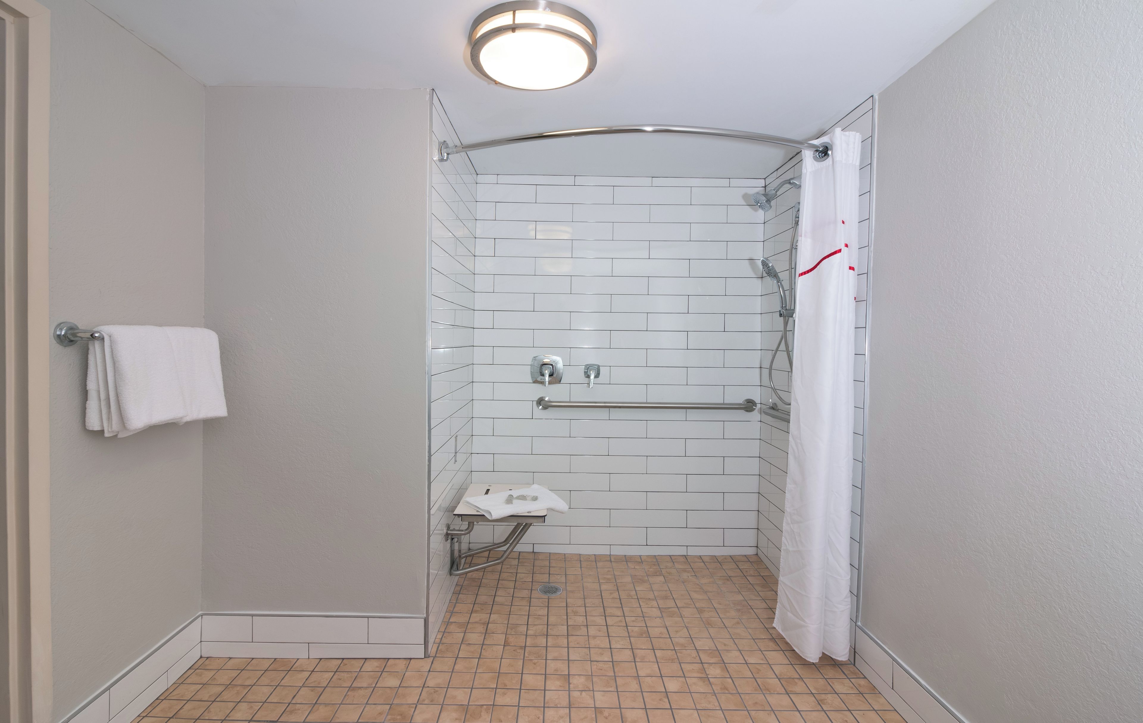 Un espacio de ducha pequeño y cerrado, con un muro cubierto de azulejos blancos, una toalla blanca colgada en la pared y una cortina de ducha blanca.