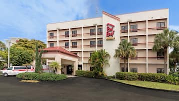 A Red Roof Plus hotel with a central entrance, multiple floors, and a parking area.
