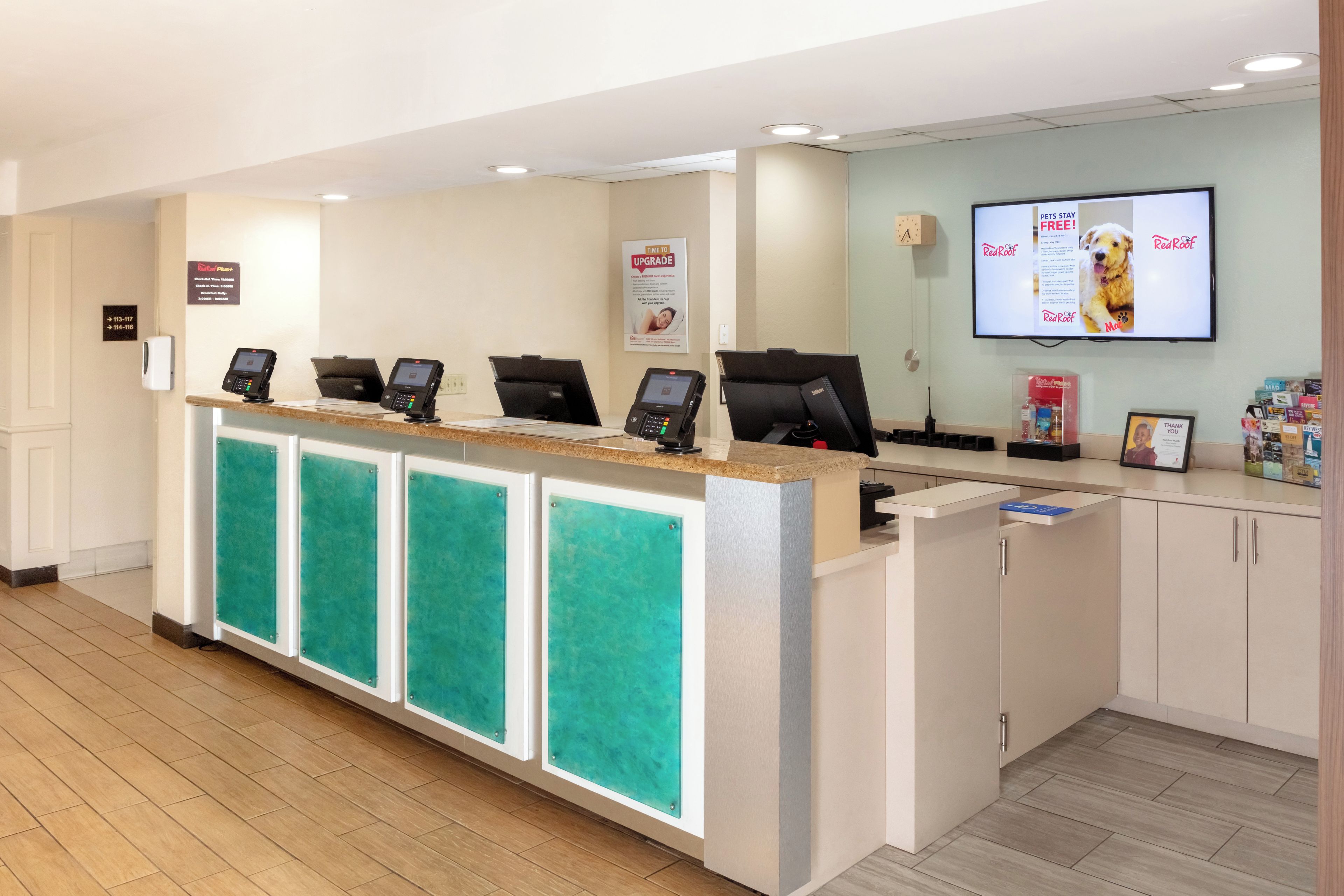 A hotel reception desk with multiple counters, a digital screen displaying pet-related content, and a sign indicating pet services are free.