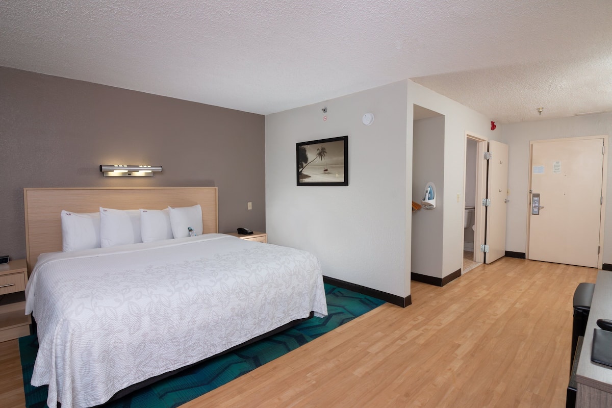 A hotel room with a large bed, a bedside table, a nightstand, a wall-mounted light, a framed picture, and a door leading to a bathroom.