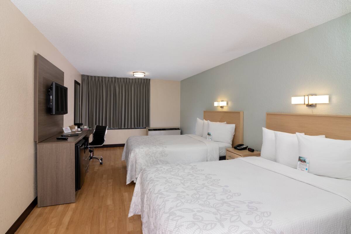 A hotel room with two beds, a desk with a TV, a chair, and a window with curtains.