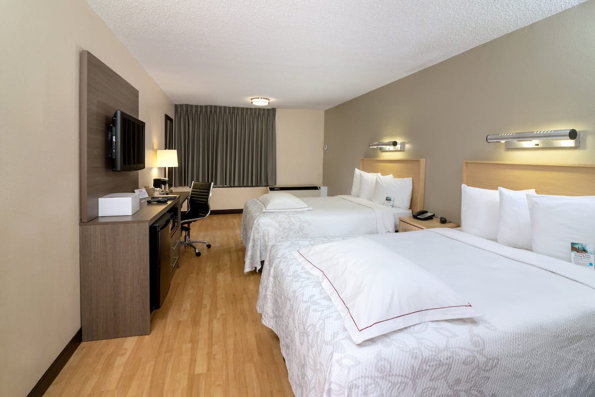 A hotel room with two beds, a desk, a TV, and a window with curtains.