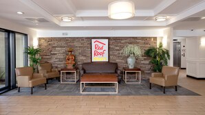 A lobby with a sofa, chairs, a red-roof sign, a statue, and a vase.