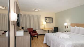 A hotel room with a bed, a desk with a chair, a television, a lamp, and a painting on the wall.