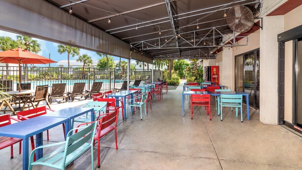 An outdoor patio area with tables and chairs, a pool in the background, and a Coca-Cola sign.