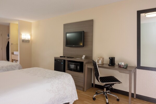A hotel room with two beds, a desk with a television, a microwave, a coffee maker, and a chair.
