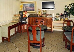 Un comedor con sillas de madera y una mesa, un televisor montado en la pared, y varios utensilios de cocina sobre la encimera.