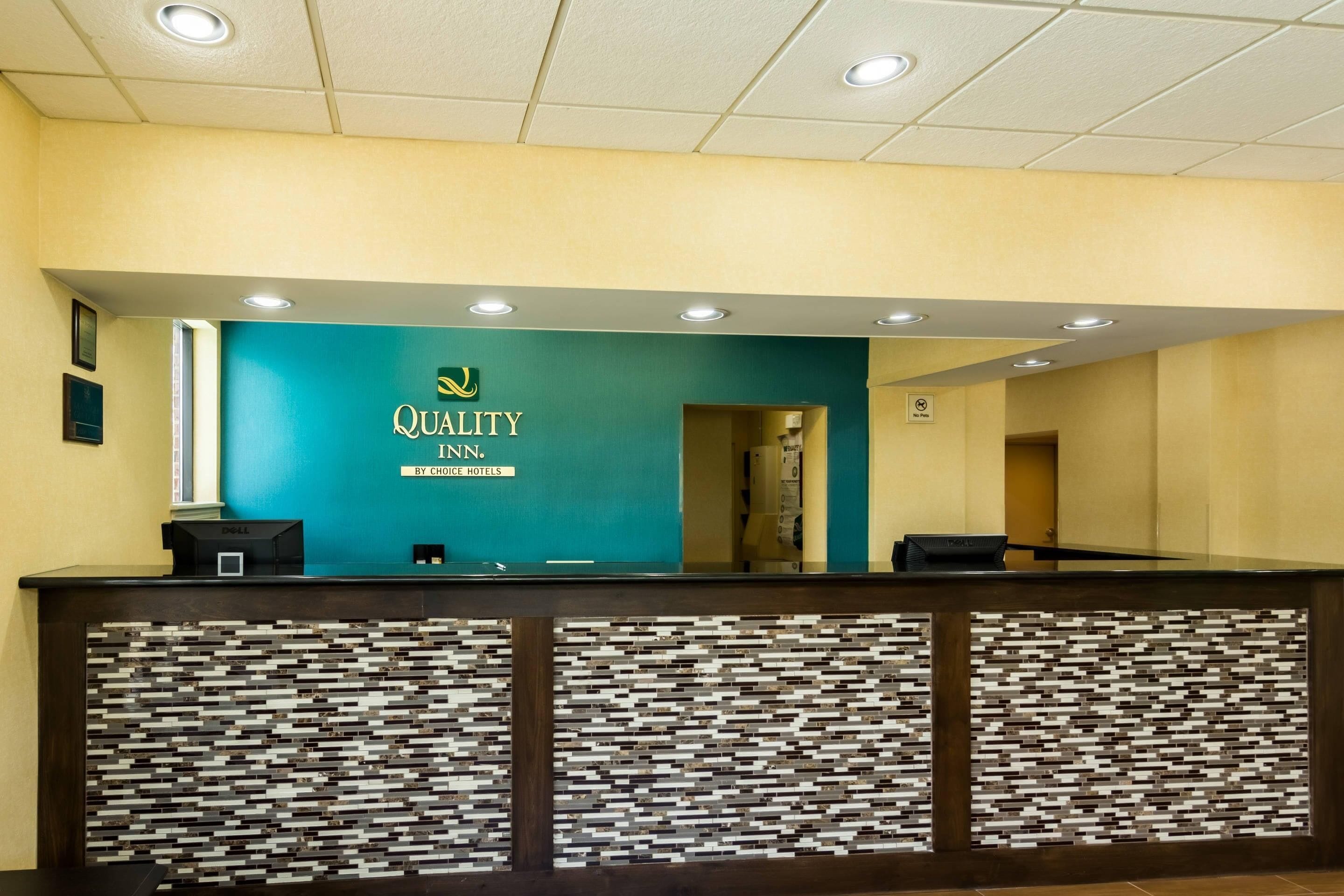 A reception desk with a teal wall and a 'Quality Inn' sign.