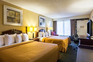Habitación de hotel con dos camas, un escritorio, una computadora, una silla y un televisor.