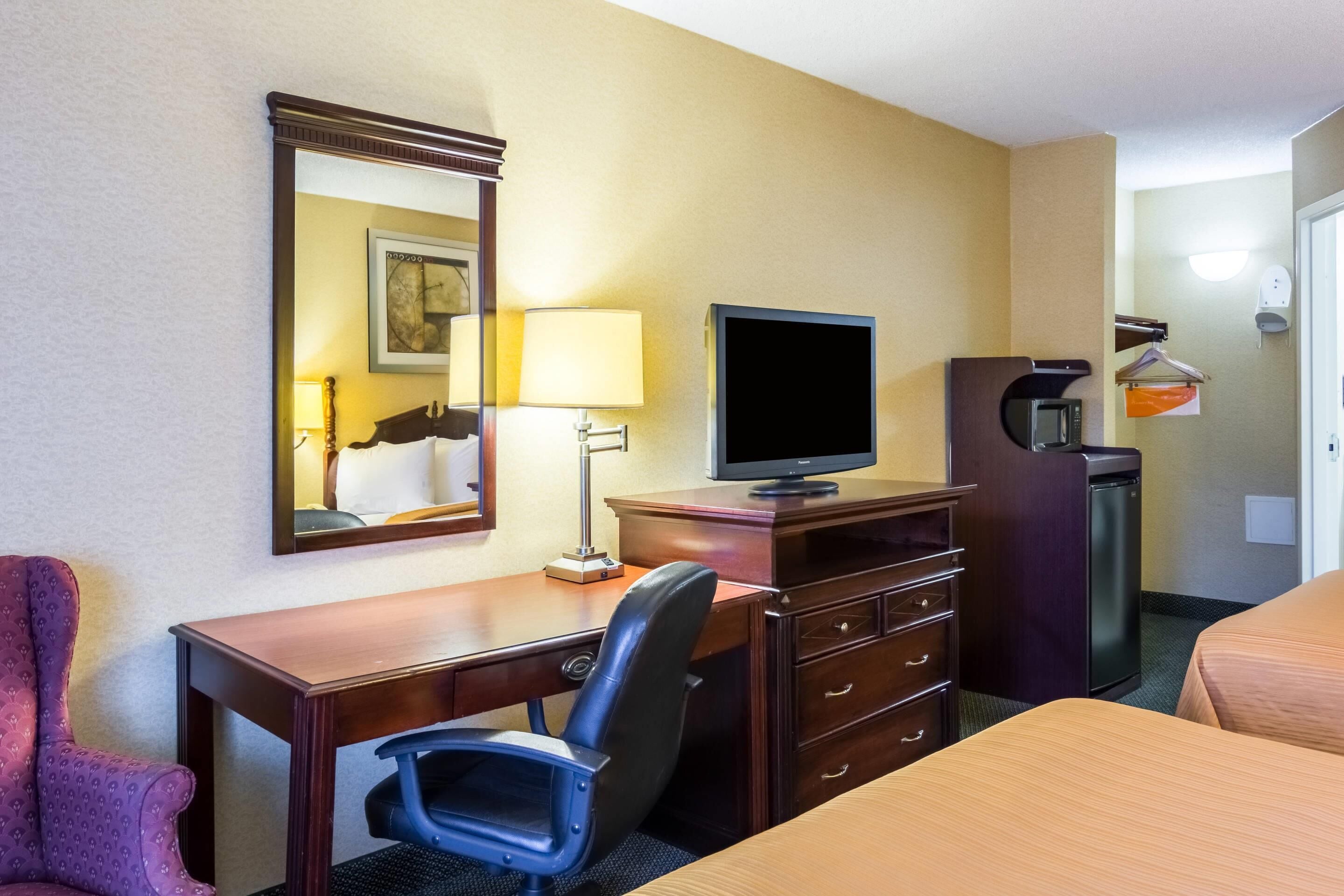 A hotel room with a wooden desk, a chair, a television, a mirror, and a wardrobe.