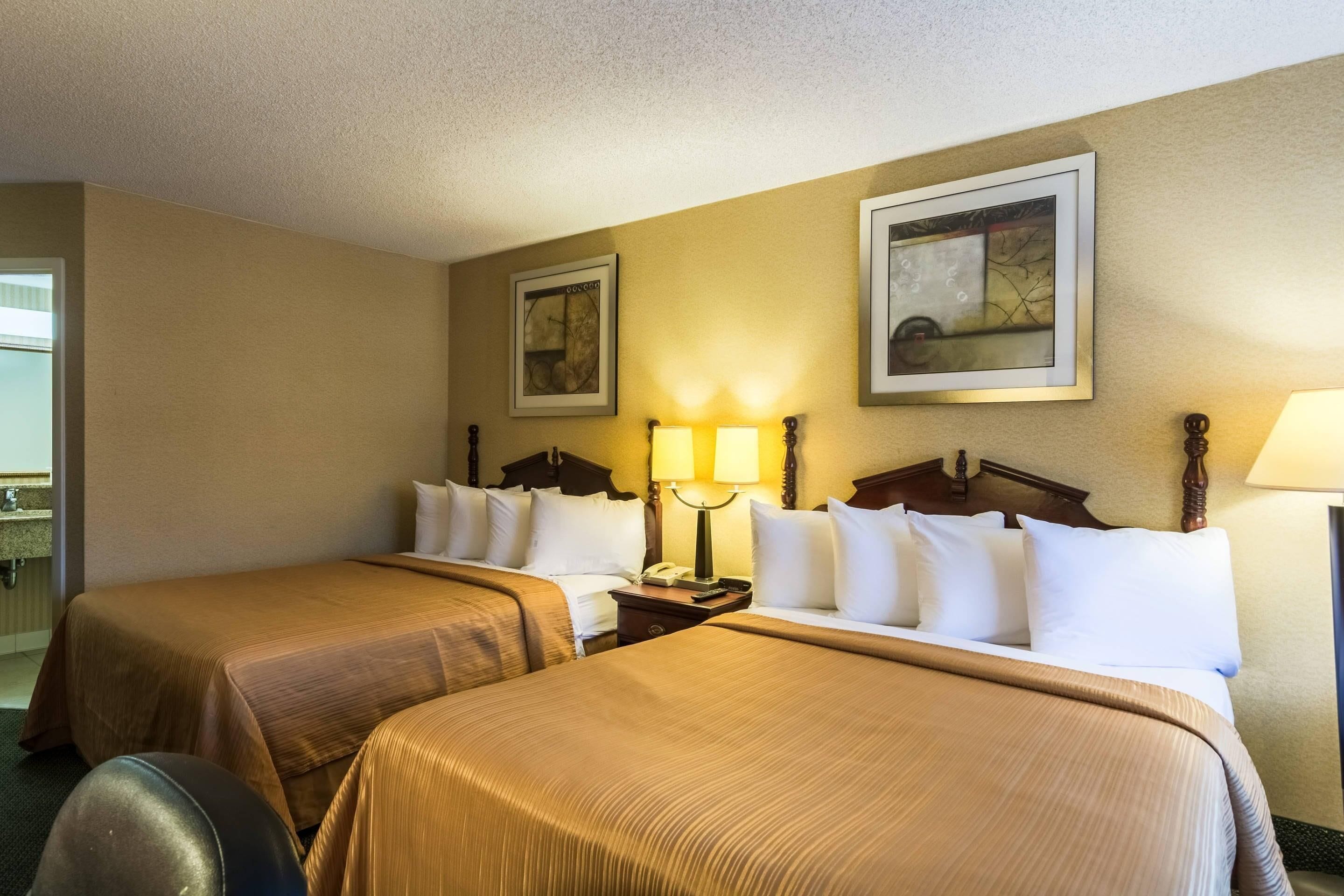 A hotel room with two beds, a nightstand, a lamp, and two framed pictures on the wall.