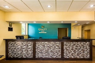 Una recepción con un letrero que dice 'Quality Inn', un letrero que indica 'No se admiten mascotas' y el logotipo de 'By Choice Hotels'.