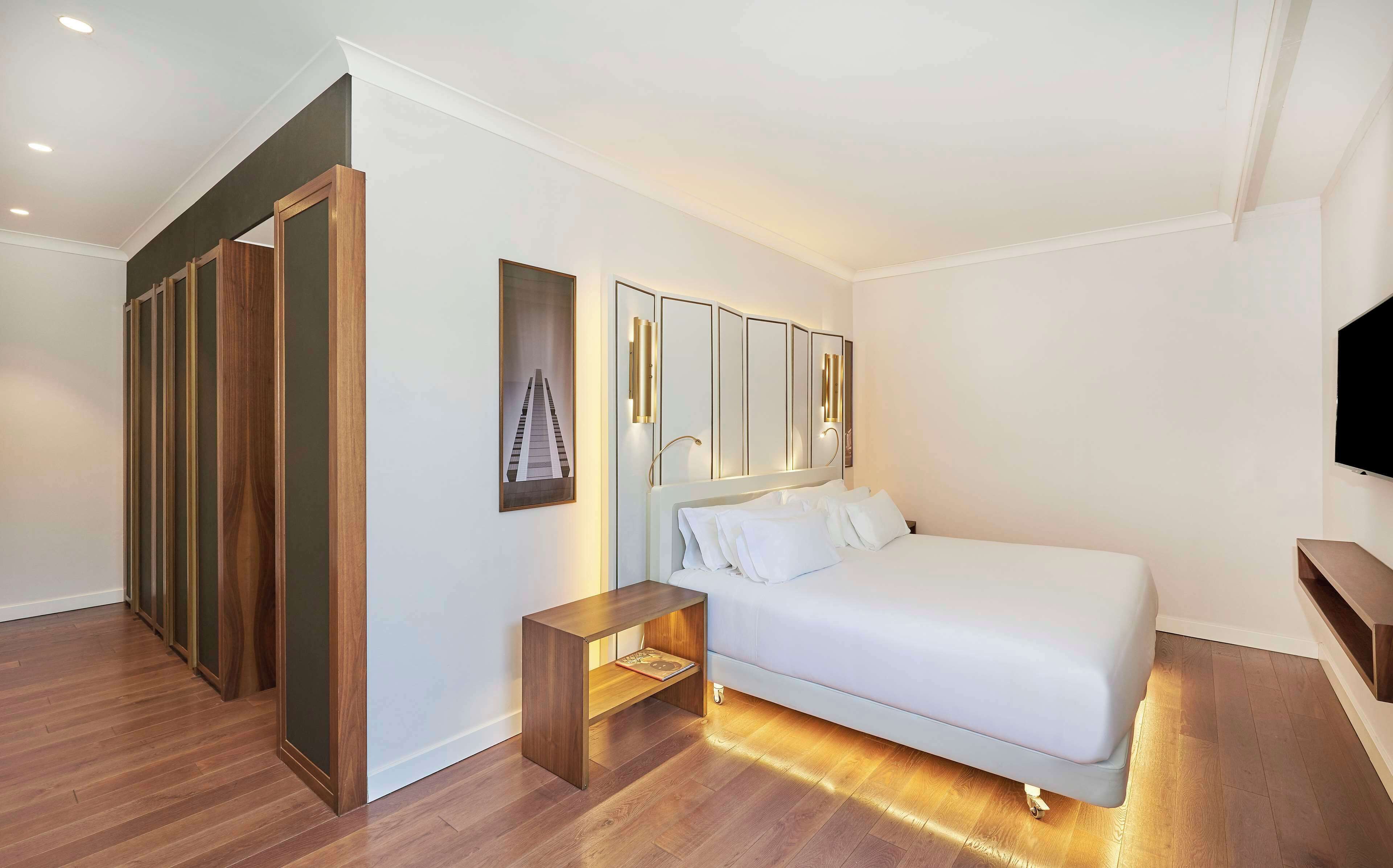 Camera d'albergo moderna con un letto grande, un armadio in legno, un piccolo comodino e una TV a muro.