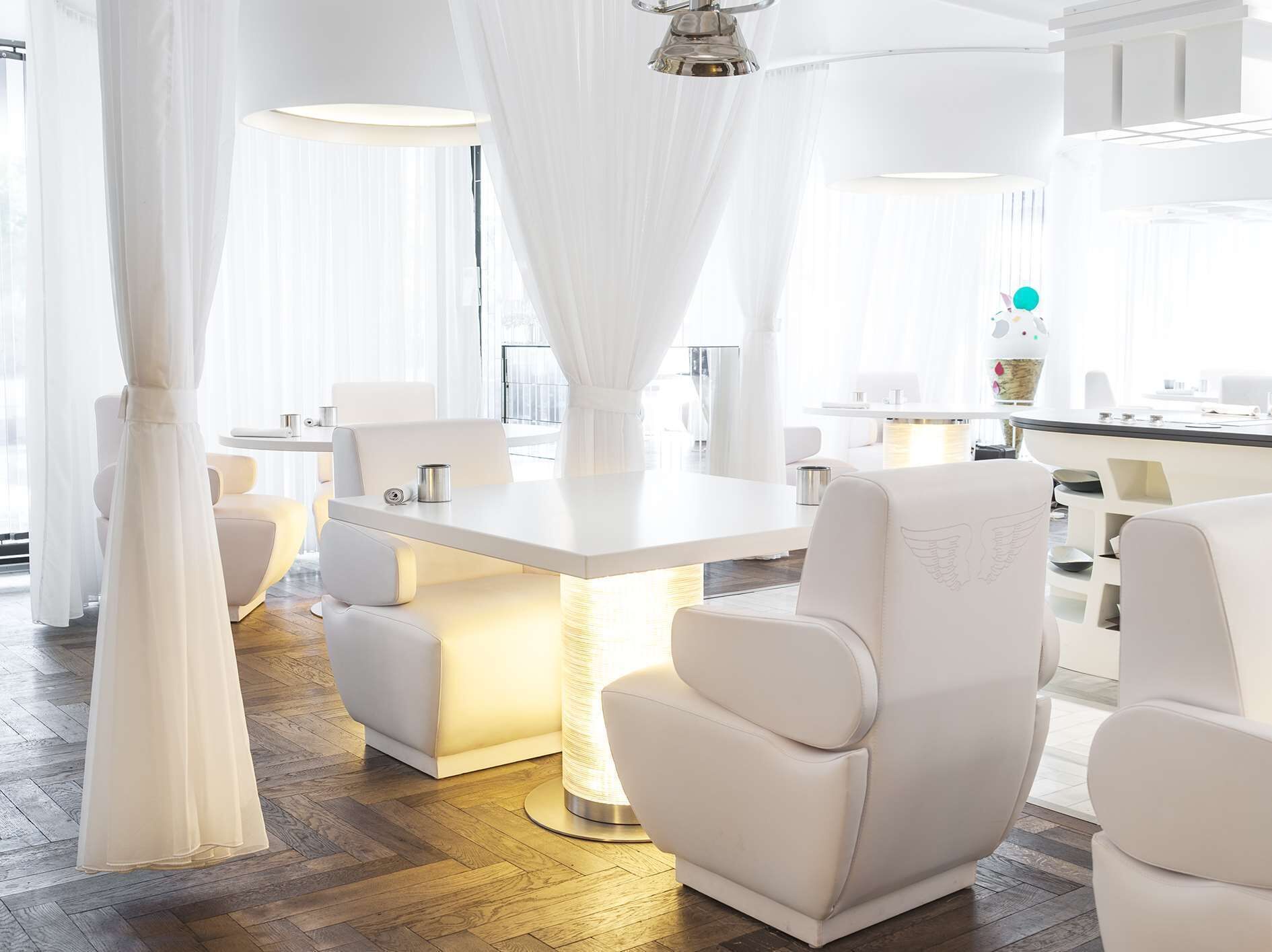 A modern, well-lit room with a central table, white chairs, and a chandelier.
