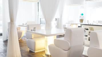 A modern, well-lit room with a central table, white chairs, and a chandelier.