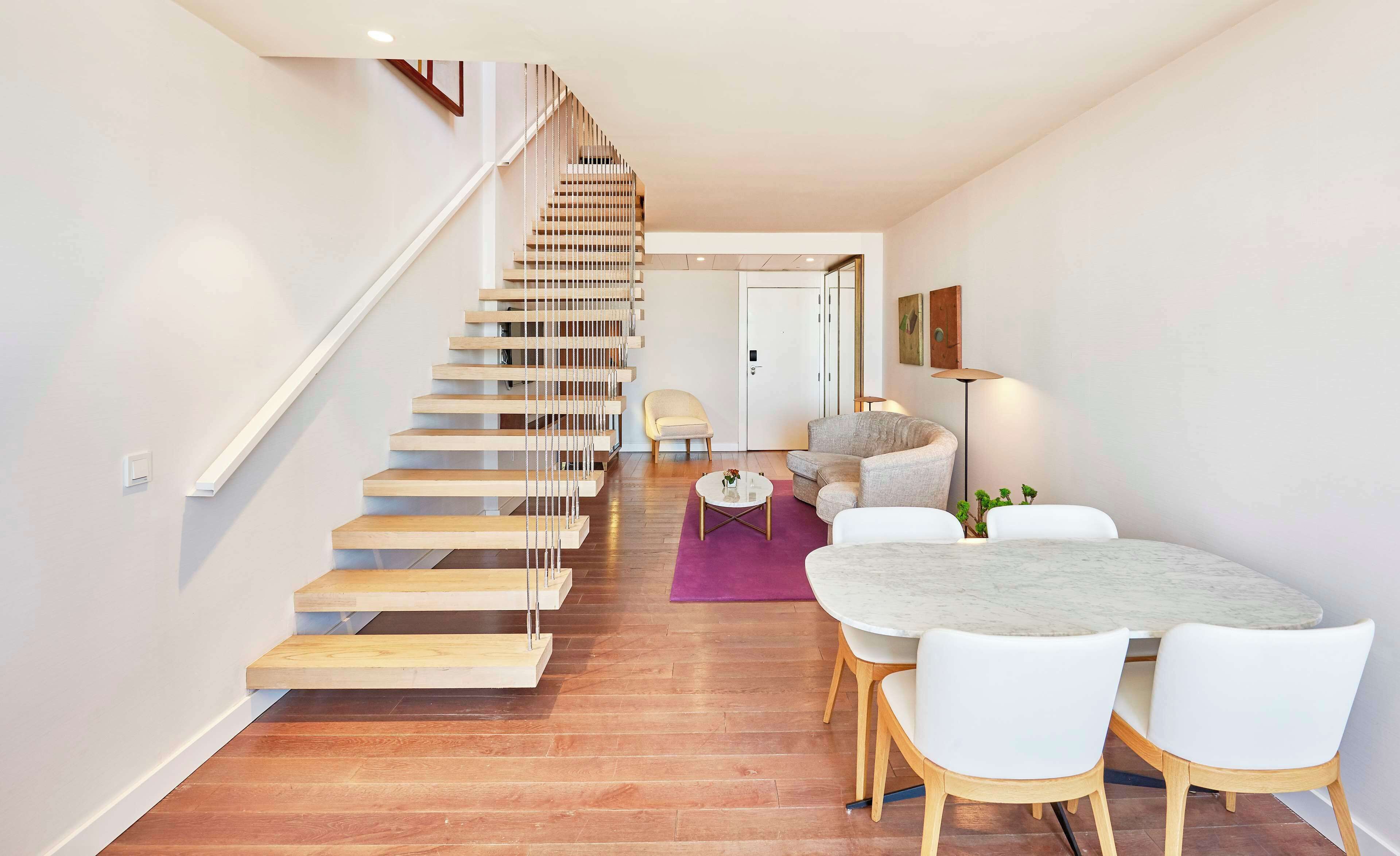 A modern interior with a wooden staircase, a dining area with white chairs, and a round table.
