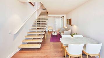 A modern interior with a wooden staircase, a dining area with white chairs, and a round table.
