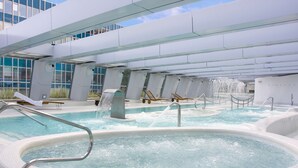 Une piscine intérieure moderne, dotée de plusieurs bains à remous et d’éléments aquatiques décoratifs, et entourée d’une architecture contemporaine.