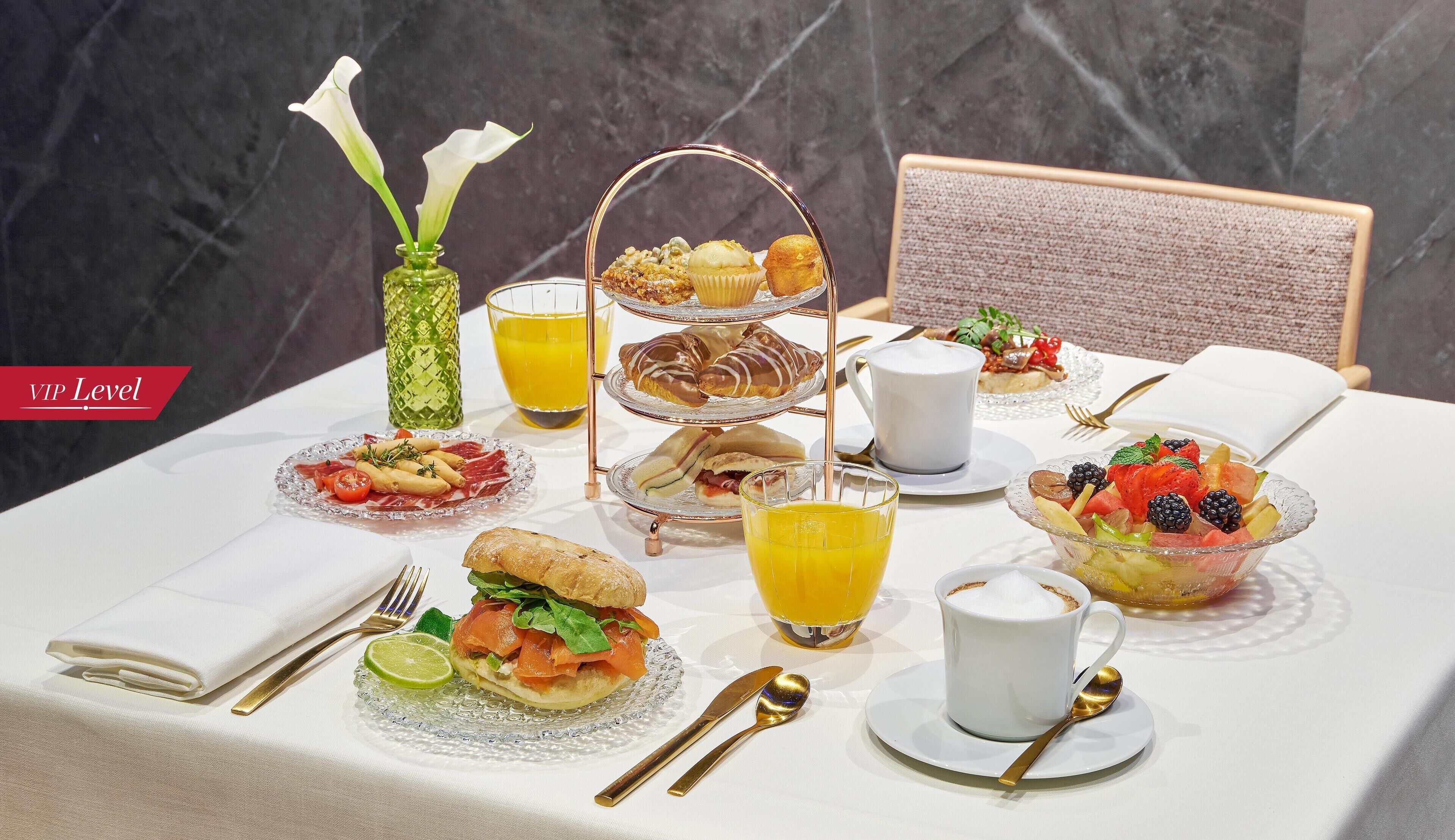 Ein Frühstückstisch mit einer Etager für Gebäck, einer Obstschale, einem Sandwich und einer Tasse Kaffee.