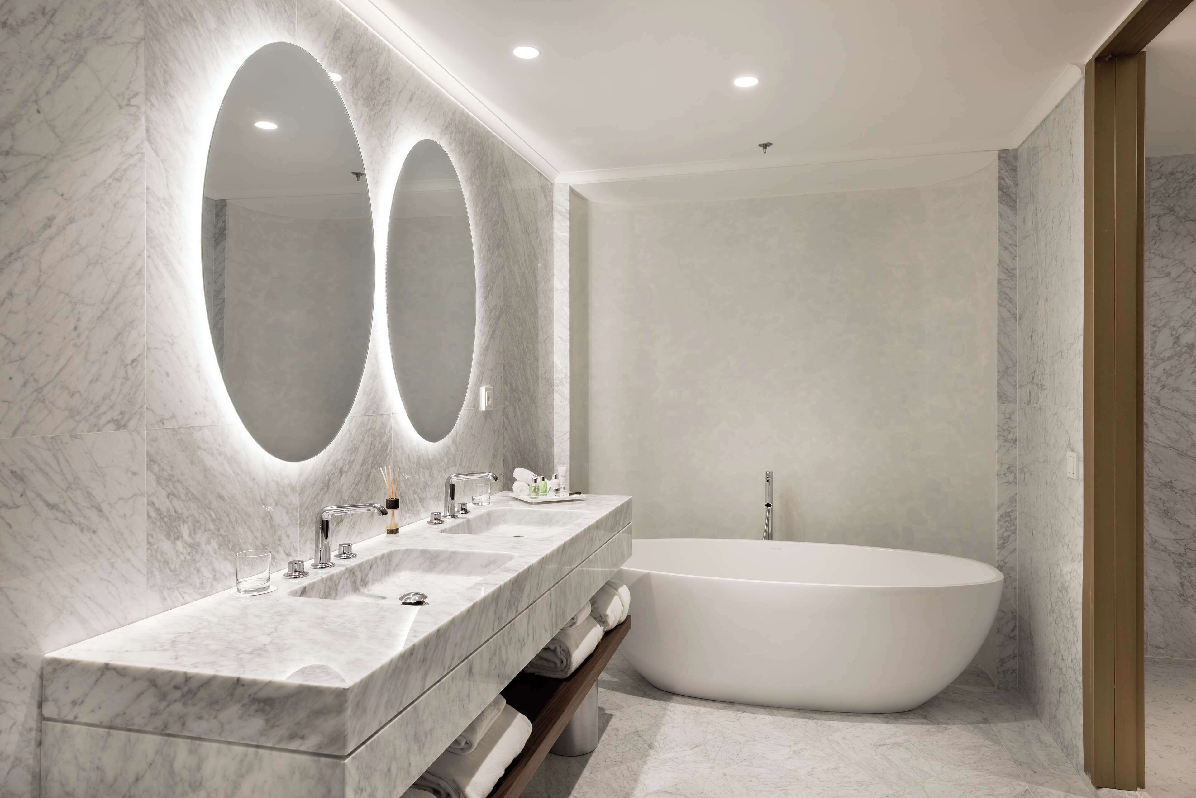 A modern bathroom with a marble vanity, two large mirrors, and a freestanding bathtub.