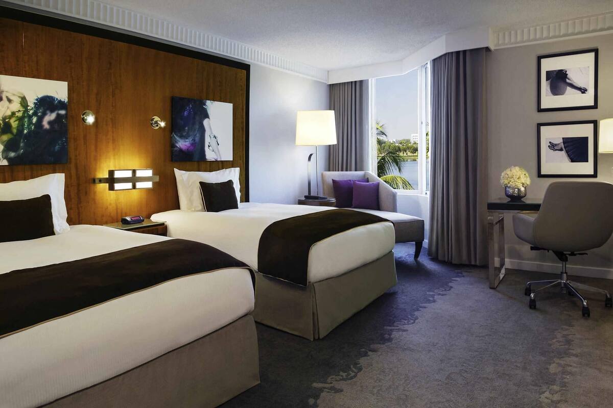 Hotellihuone, jossa on kaksi sänkyä, työpöytä, tuoli ja taideteoksia seinillä.