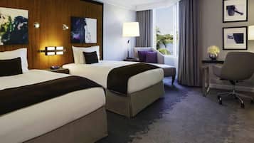A hotel room with two beds, a desk, a chair, and artwork on the walls.