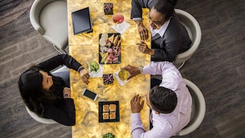 Vista cenital de una sala de reuniones con una mesa de mármol, sillas y varios objetos, entre ellos una tableta, teléfonos inteligentes y comida.