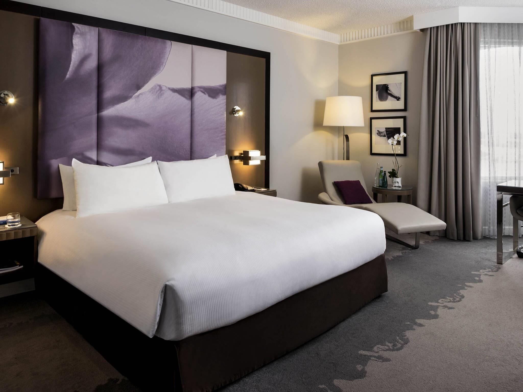 A hotel room with a large bed, a chair, a desk, and a lamp.