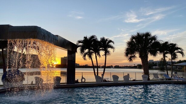 A pool area with a water feature, palm trees, and a sunset view. - Pullman Miami Airport (Miami)