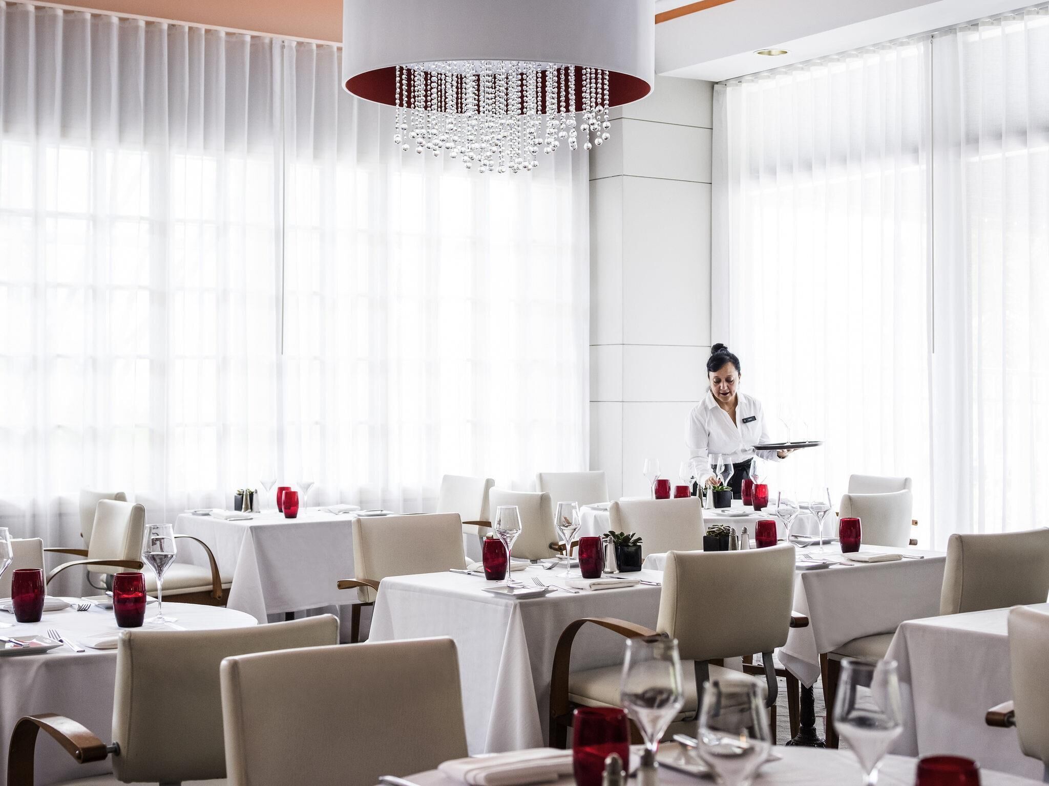 Een restaurant met gedekte tafels, een ober die gasten bedient en een kroonluchter.