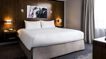 Une chambre d’hôtel avec un grand lit, deux tables de chevet avec des lampes, un téléviseur fixé au mur et une fenêtre avec des rideaux.
